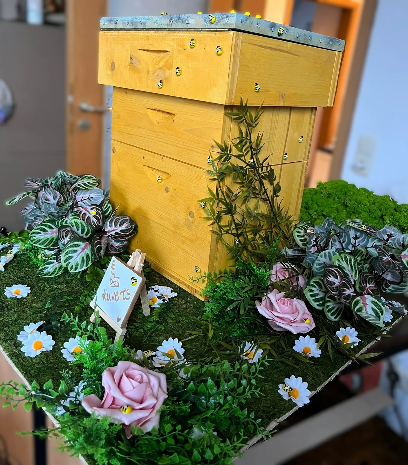 Dekorativer Bienenstock-Aufbau mit Kunstblumen und Moos als Gastgeschenktisch